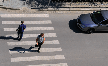 duas pessoas atravessando a faixa de pedestre e carro cinza parado na via.