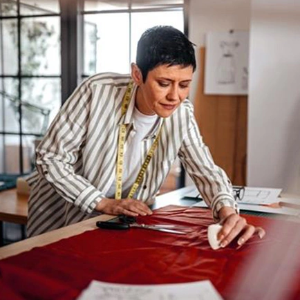 Costureira riscando tecido vermelho em uma mesa de trabalho.