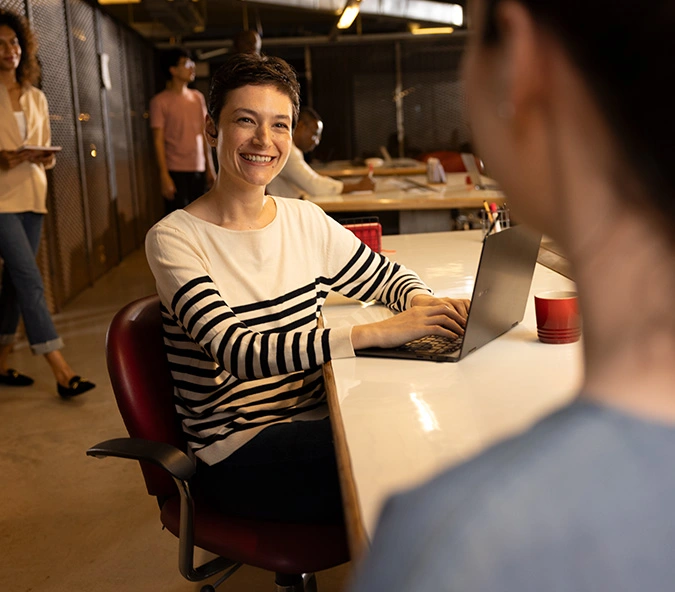 Mulher sorrindo enquanto trabalha em um laptop em escritório.